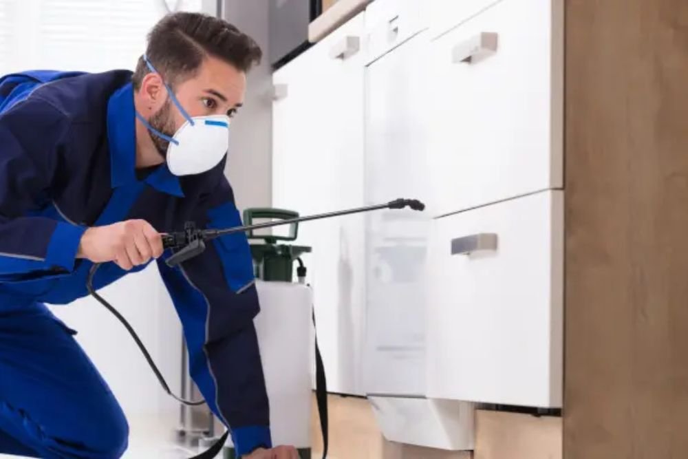 A man in blue overalls uses a sprayer for pest control, illustrating a home pest control service in Las Vegas, NV.