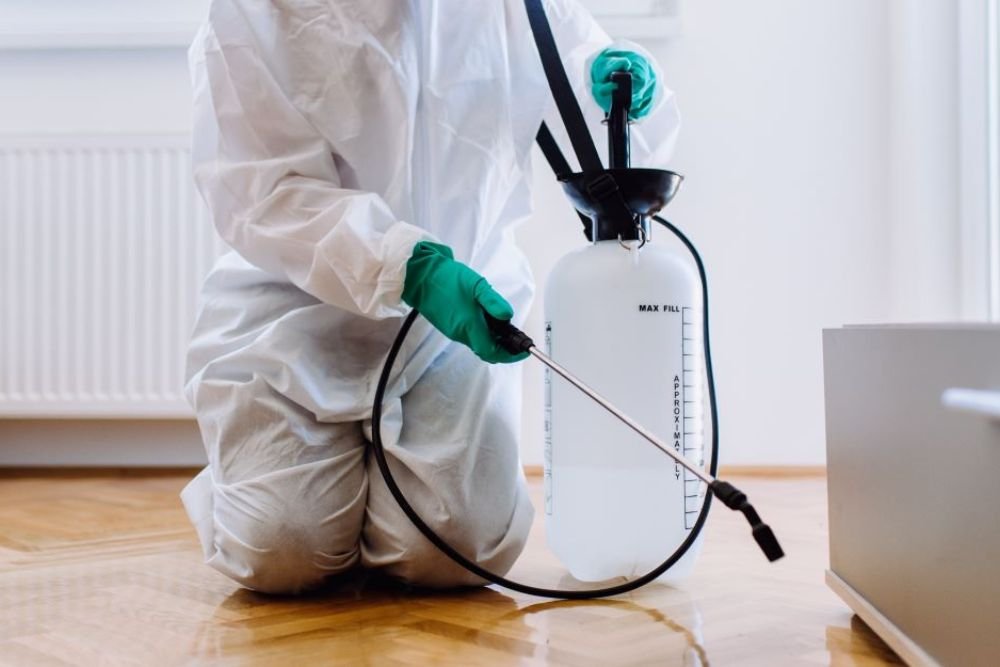 A person wearing a white coat and gloves applies pest control spray in a Las Vegas neighborhood, ensuring effective pest management.